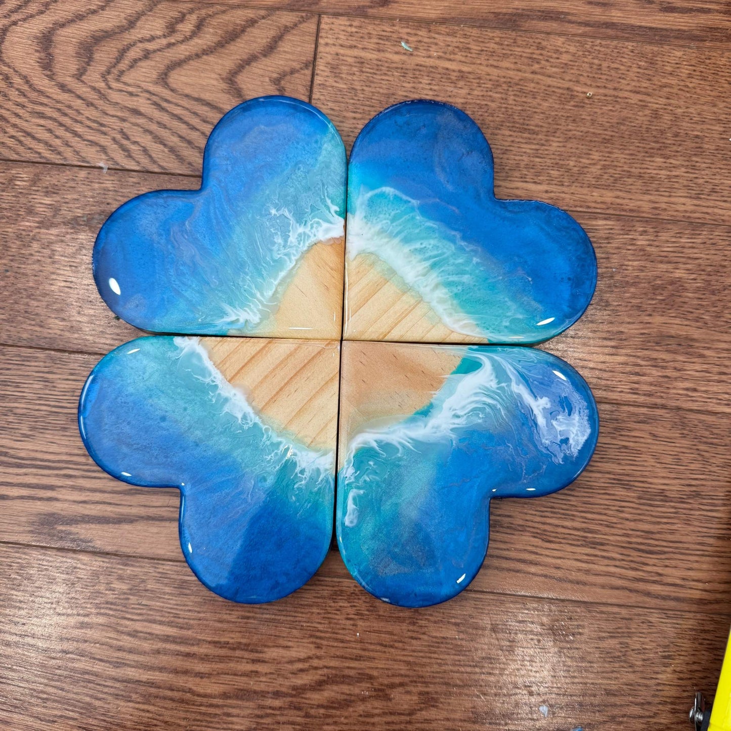 Set of four heart-shaped resin coasters with ocean wave design and glossy finish on wooden surface
