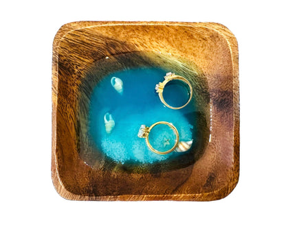 Square wooden jewelry plate with deep sea inspired blue resin center holding two gold rings
