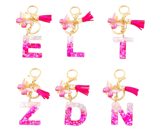 Pink resin alphabet keychains with gold rings, pink tassels, and butterfly charms in letters E, L, T, Z, D, and N