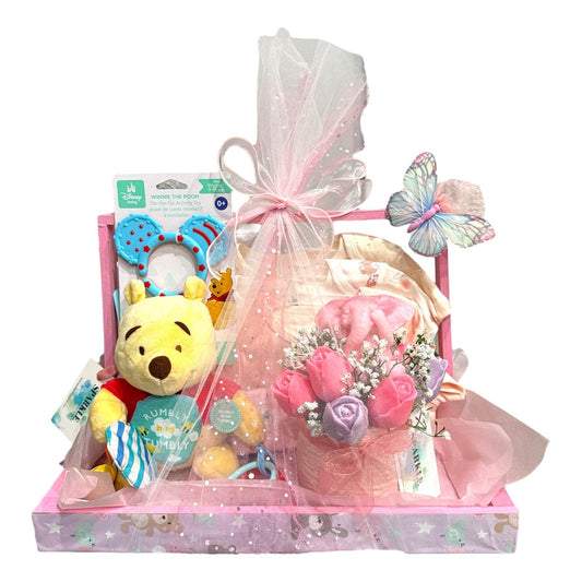 Customizable gift basket for mom with baby clothes, blanket, shea soap, candle, bouquet, and plush toy wrapped in pink packaging