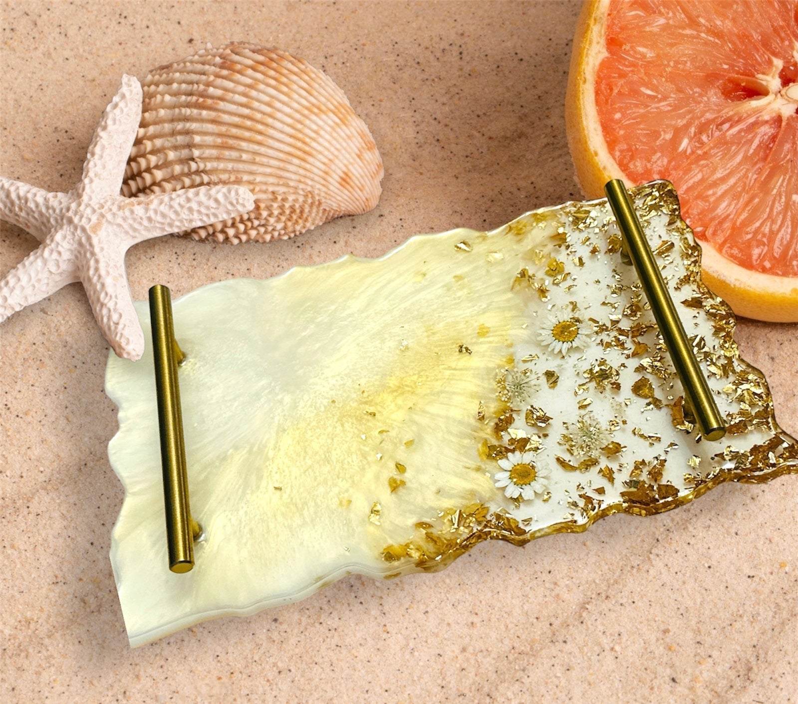 Handmade resin decorative tray with embedded real dried flowers and gold flakes, featuring brass handles on a sandy background with seashells and grapefruit slice.