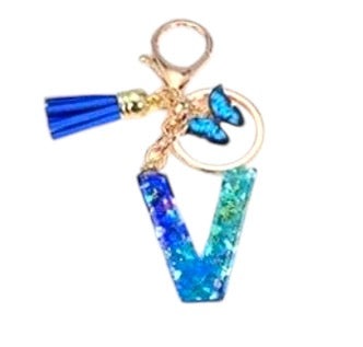 Blue resin alphabet keychain with glitter effect, butterfly charm, and blue tassel attached to a gold metal ring