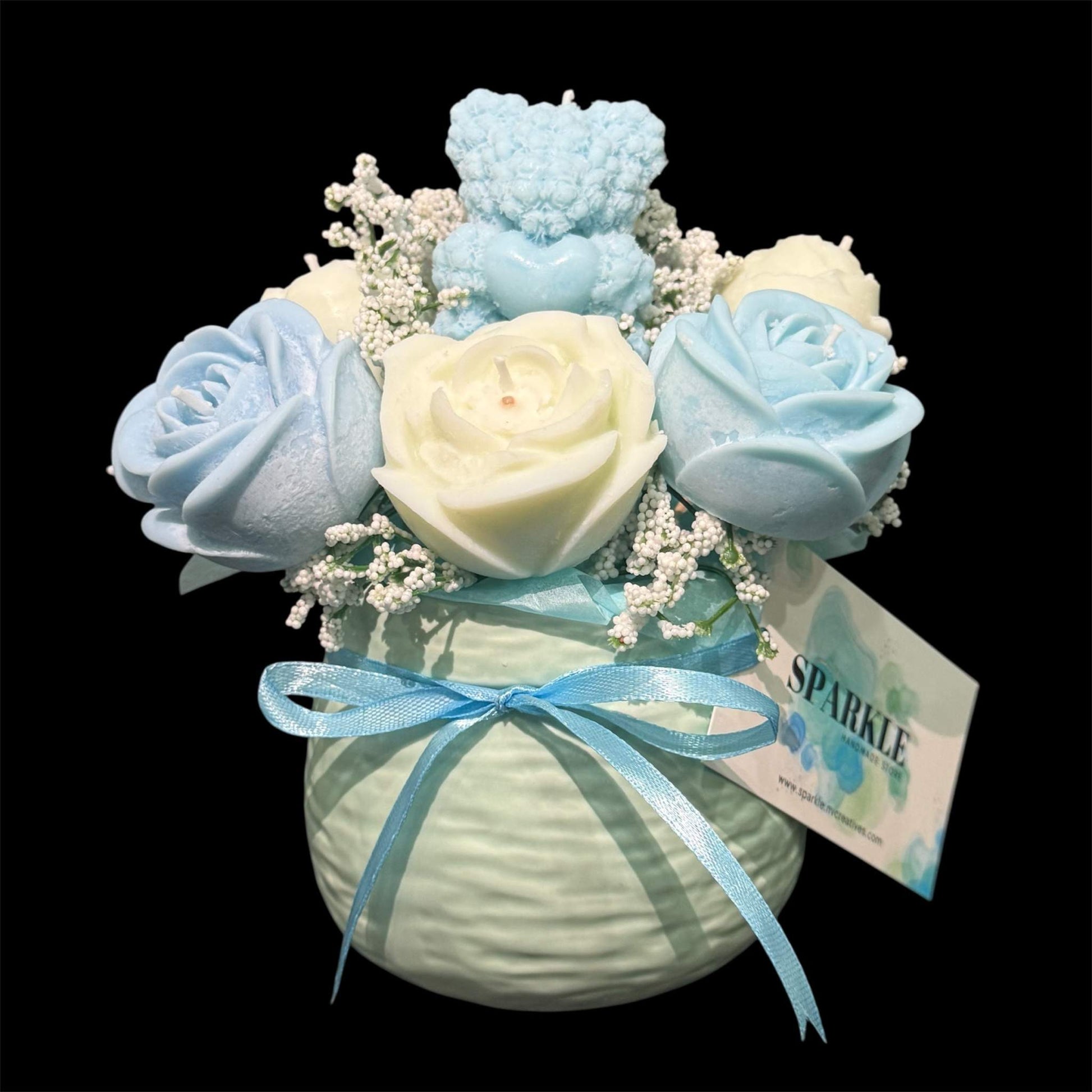Handmade scented candle flower bouquet with blue and cream rose-shaped candles, blue teddy bear candle, white baby's breath accents, in a round vase with blue ribbon decoration