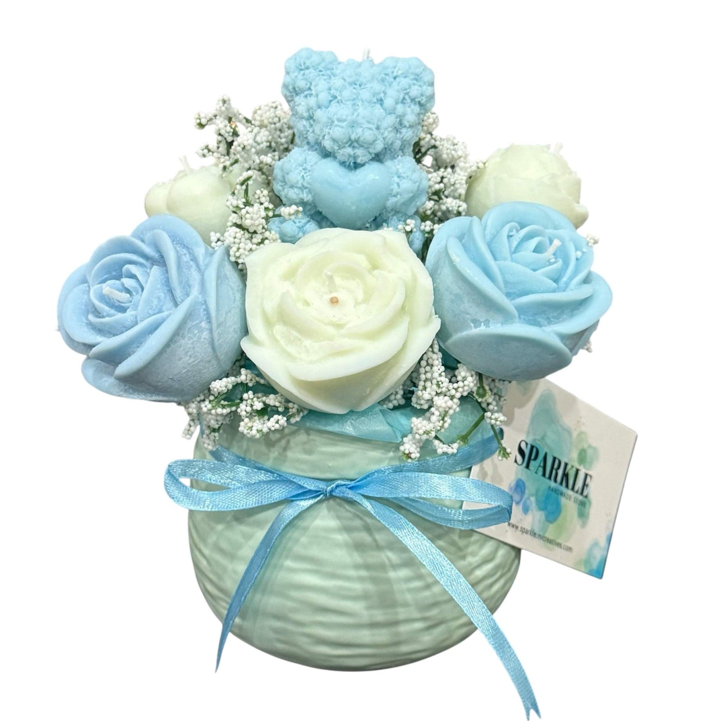 Handmade candle flower bouquet with blue and cream rose-shaped candles, baby’s breath, and a blue teddy bear candle in a decorative round vase with blue ribbon.