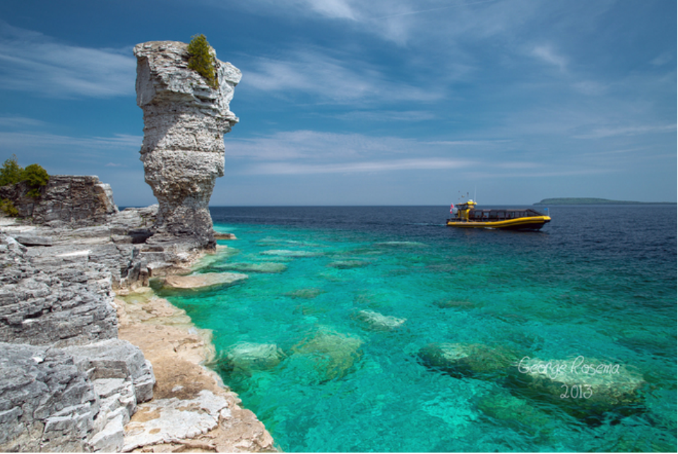 crystal-clear turquoise waters and rocky cliffs of Flowerpot Island coastal landscapes art with boat on ocean under blue sky