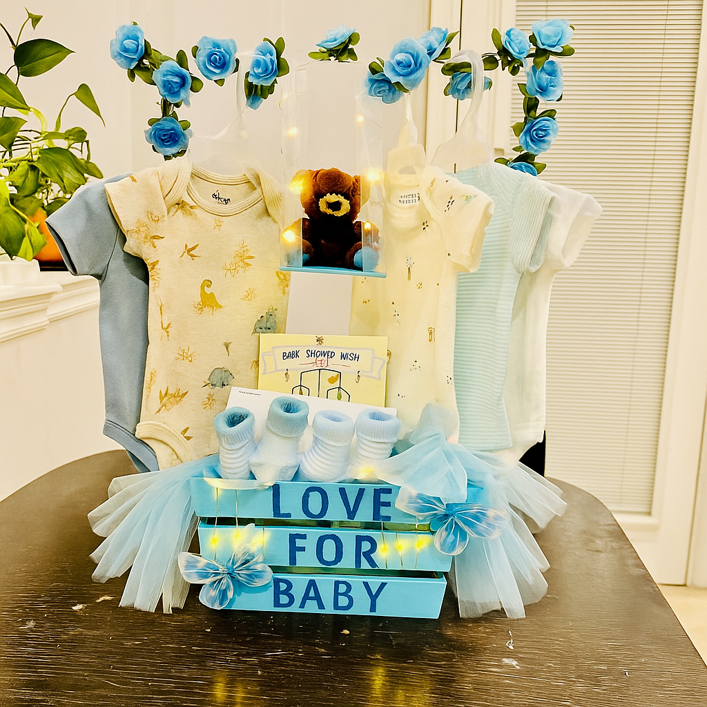 Custom baby shower gift basket with handmade newborn essentials including blue-themed onesies, socks, a plush teddy bear, and decorative blue flowers.
