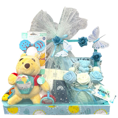 Customizable gift basket for mom with baby clothes, blanket, shea soap, candle, bouquet, and plush toy in blue-themed packaging
