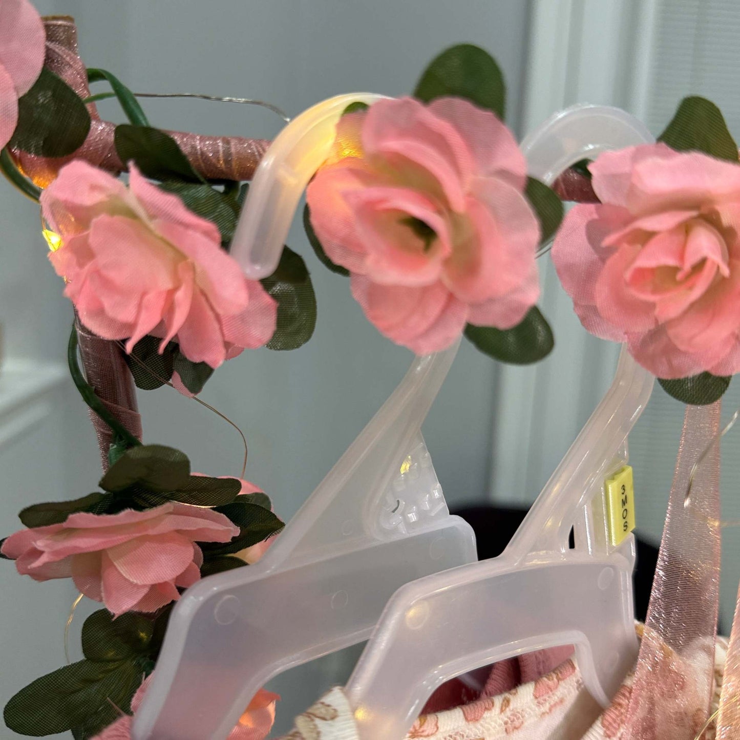 Plastic baby clothes hangers decorated with pink artificial flowers, part of a custom baby shower gift basket setup