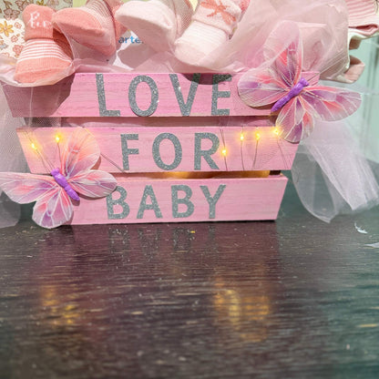 Pink wooden crate with "Love for Baby" text, decorated with butterflies, fairy lights, and baby socks, part of a custom baby shower gift basket.