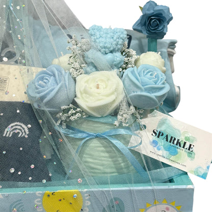Customizable gift basket for mom with blue and white baby clothes, blanket, shea soap, hand-poured candle, and mini floral bouquet.