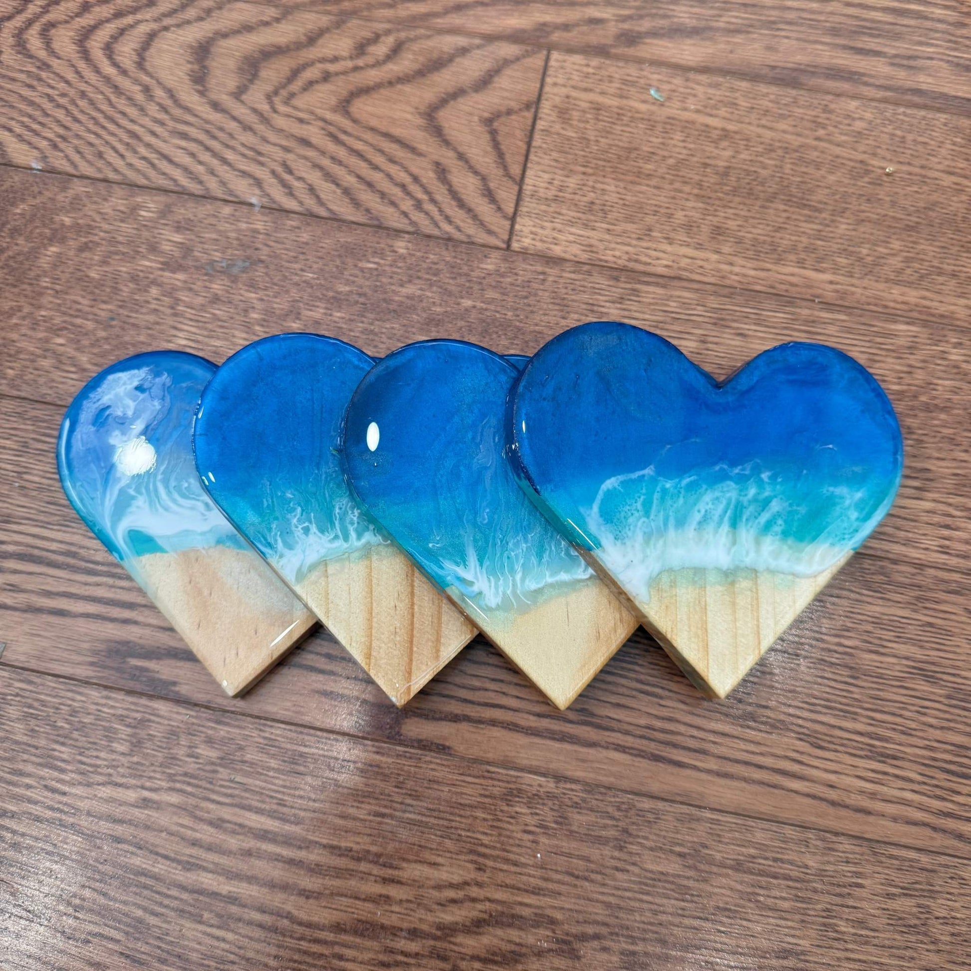 Set of handmade heart-shaped ocean wave resin coasters with glossy finish and cork backing on wooden surface