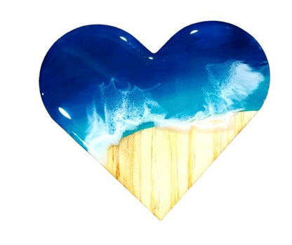 Heart-shaped ocean wave resin coaster with blue and white wave design over wooden texture surface