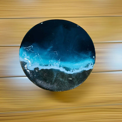 Round ocean art with black sand and blue waves on wooden board
