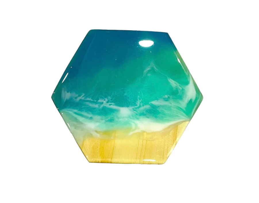 Hexagonal handmade ocean wave resin coaster with blue and white wave design over a sandy wood base