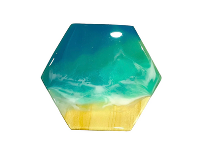 Hexagonal handmade ocean wave resin coaster with blue and white wave design over a sandy wood base